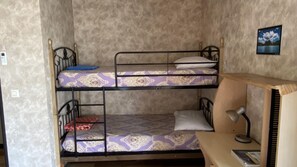 Une chambre avec un lit superposé, une literie à motifs, un bureau avec une lampe et un tableau encadré au mur.