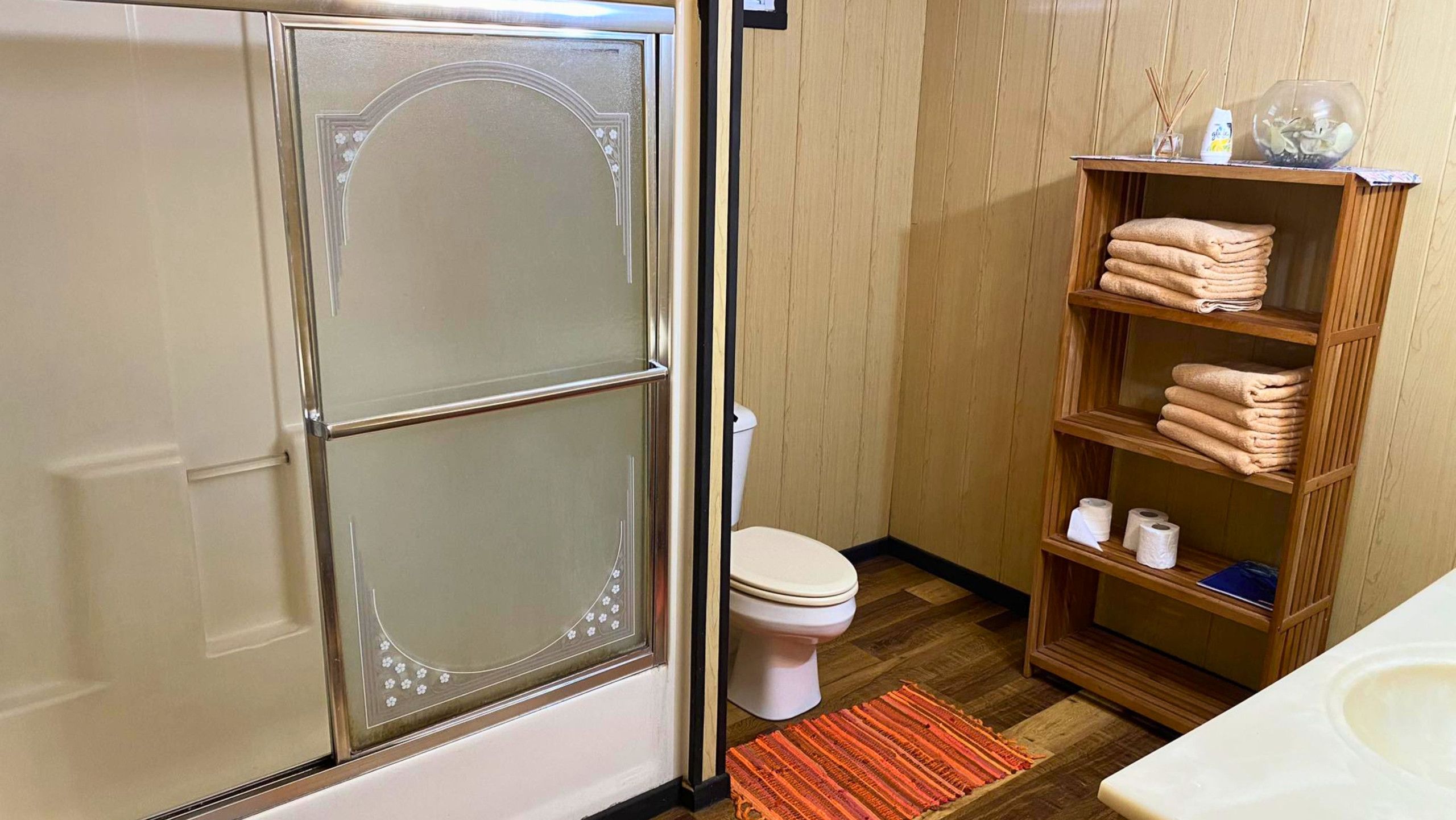 A bathroom with a toilet, a shelf with towels, and a wooden cabinet.