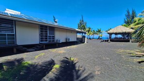 A building with a solar panel roof, a covered outdoor seating area, and a thatched structure. - TAHITI - Taharuu Bungalow Surf Piti (Papara)