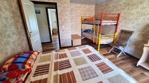 A room with bunk beds, a single bed with a floral comforter, a wooden chair, and a small table. - TAHITI - Taharuu Bungalow Surf Piti (Papara)