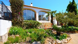 A Mediterranean-style villa with a white facade, terracotta roof, and a garden with various plants and flowers. - Belle Villa Avec Piscine 5 x 10 m, Grand Jardin Privatif, Proche des Plages (JAVEA)