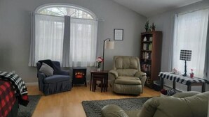 A living room with a fireplace, two armchairs, a bookshelf, and a window with curtains.