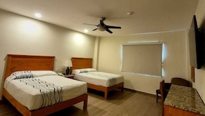 Una habitación de hotel con dos camas, un ventilador de techo, un escritorio y un televisor.