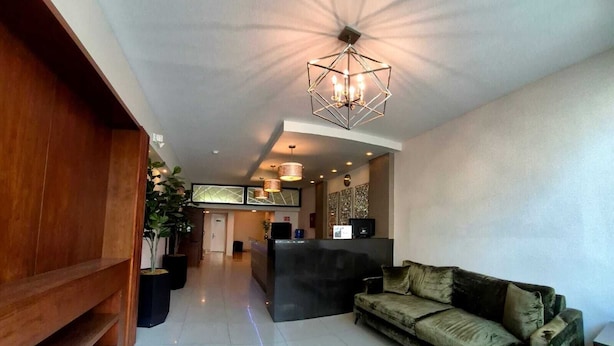 Amplia sala de estar con un sofá moderno, un banco de madera, un mostrador de recepción y un moderno aplique de techo geométrico.