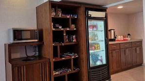 Una kitchenette con microondas, un refrigerador y estantes de madera con diversos objetos.