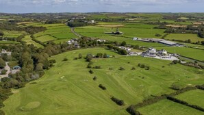 An aerial view of a rural area with green fields, a few scattered buildings, and a large open space that could be a park or sports field. - Wheal Amelia Lodge (Helston)
