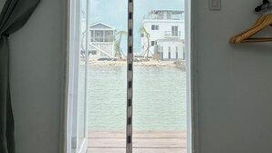 Ein Zimmer mit einer Schiebeglastür, die auf ein Holzdeck mit Blick auf ein Gewässer und Gebäude führt.
