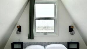 Ein raumförmiges Zimmer mit einem Bett, zwei Nachttischen, einem Fenster und einer Wandleuchte.