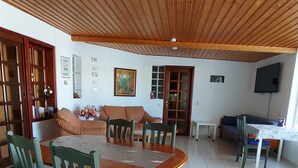 Zona pranzo con tavolo e sedie in legno, un divano e una televisione sullo sfondo.