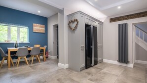 A modern kitchen with grey cabinets, a stainless steel refrigerator, and a dining area with a table and chairs. - Bridge Howe (Ambleside)