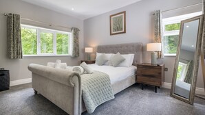 A bedroom with a large bed, two bedside tables, a mirror, and a window with curtains. - Bridge Howe (Ambleside)