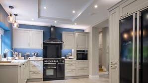 A modern kitchen with white cabinets, a black stove, and a large refrigerator. - Bridge Howe (Ambleside)