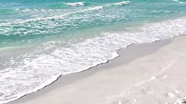 Ein Strand mit klarem türkisblauem Wasser und einem weiten, sandigen Ufer.