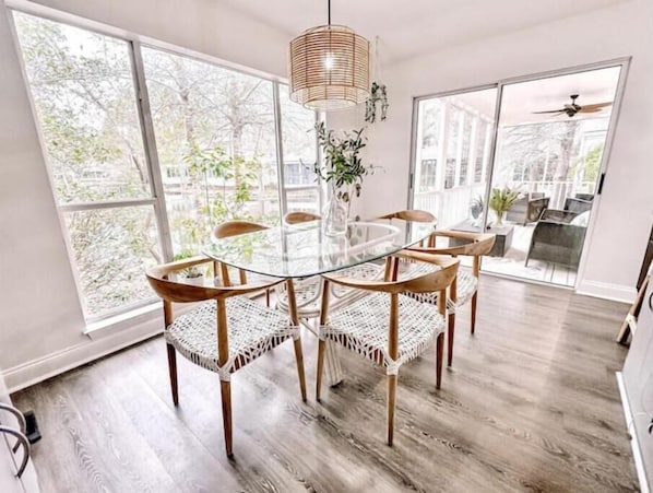 A dining area with a glass table surrounded by wicker chairs, large windows, and a ceiling fan.