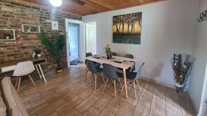Een eetruimte met een houten tafel en stoelen, een plafondventilator en een bakstenen muur.