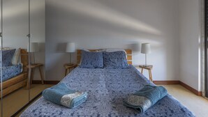 A bedroom with a large bed, two bedside tables with lamps, a mirror, and a wooden headboard. - Global Guest Sintra (Sintra)