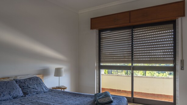 A bedroom with a bed, a nightstand, a lamp, and a view through a sliding door to an outdoor balcony. - Global Guest Sintra (Sintra)