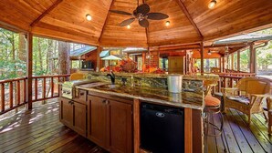 Una terraza de madera con área de cocina, que incluye un lavabo, gabinetes y un lavavajillas.