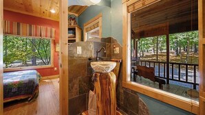 Un baño con tocador de madera, un lavamanos con una cuenca de piedra singular y una ventana con vista a árboles.