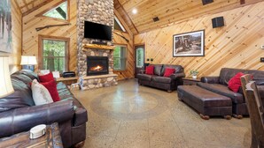 A spacious living room with a stone fireplace, leather sofas, and a television mounted on the wall.