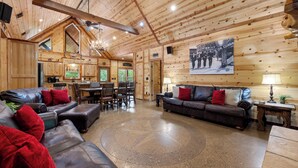 A spacious living area with a high ceiling, wooden walls, a large dining table, and a cozy seating arrangement.