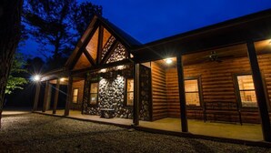 A log cabin with a stone wall entrance, wooden beams, and a covered porch with benches.