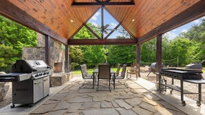 An outdoor patio with a stone floor, a grill, a table with chairs, and a ceiling fan.