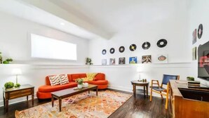 A modern living room with a red sofa, a coffee table, and a rug. There are wall-mounted records and framed pictures. - Retro Vibes - King Bed - Long Stays - Garage - Wi-Fi!
 (Edmonton)