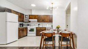 A modern kitchen with wooden cabinets, white appliances, and a dining area with two chairs and a table set for two. - Retro Vibes - King Bed - Long Stays - Garage - Wi-Fi!
 (Edmonton)