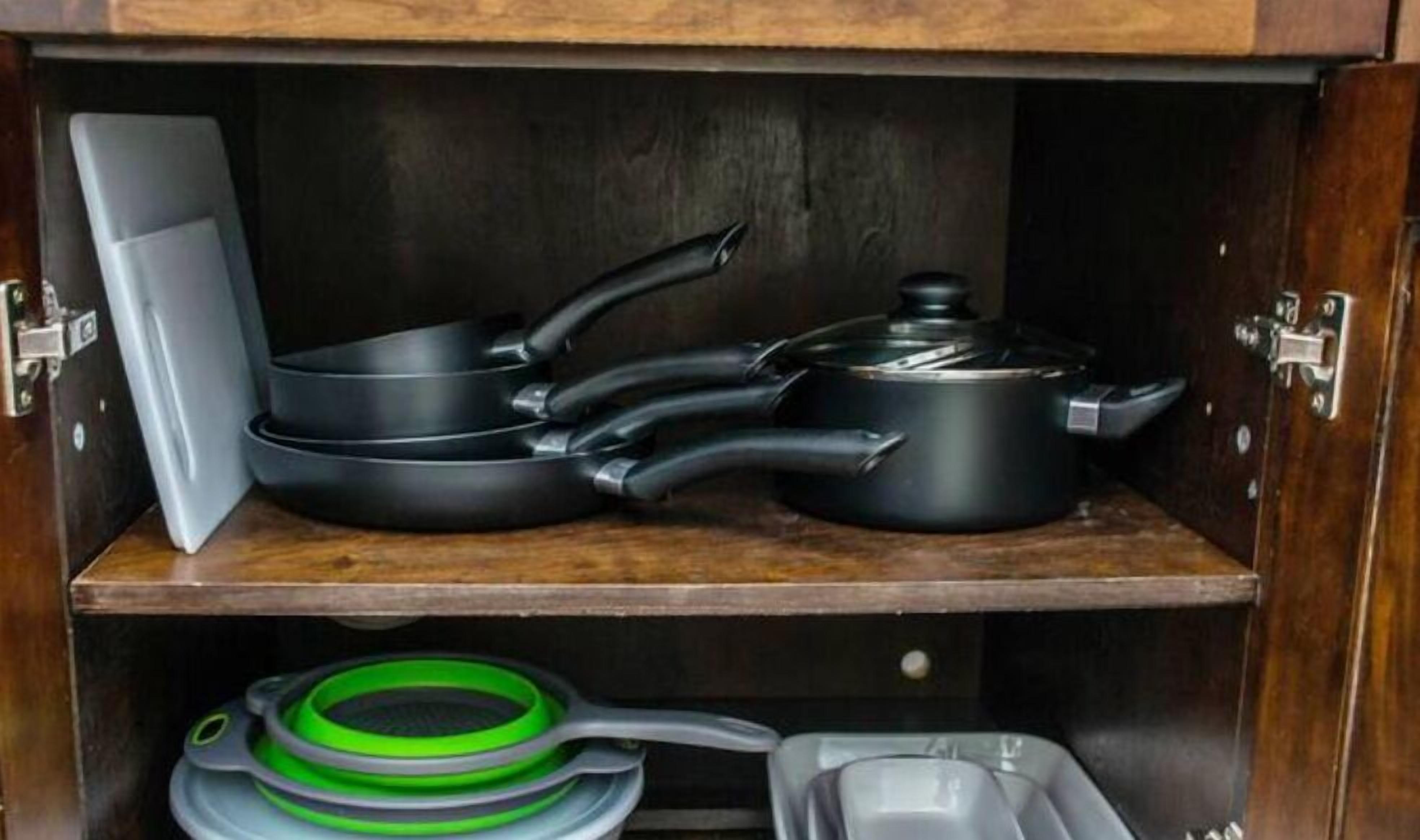 A kitchen with a wooden cabinet containing cookware, including a frying pan, a pot, and a saucepan.