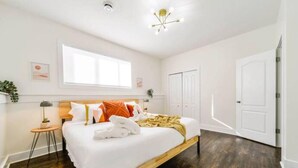 A bedroom with a bed, a window, a door, and a small table with a lamp. - Retro Vibes - King Bed - Long Stays - Garage - Wi-Fi!
 (Edmonton)
