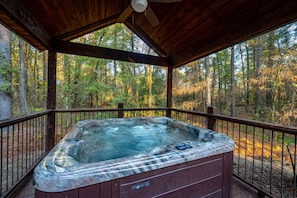 Relax in a hot tub on a deck surrounded by a serene forest view.