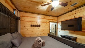 A wooden cabin room with a bed, a ceiling fan, a mounted TV, and a wooden dresser. - Fall in love with Legends Of The Fall cabin. Play Games & Soak in Large Hot Tub! (Broken Bow)