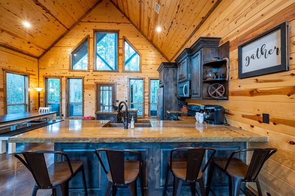 Enjoy expansive forest views from the large windows of this cabin, featuring a central island with bar stools and modern amenities.