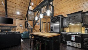 Un interior de cabaña acogedor con detalles de madera, una chimenea de piedra, un televisor grande, una cocina con electrodomésticos modernos y una zona de bar.