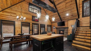 Interior acogedor de una cabaña con detalles de madera, una chimenea de piedra, una zona de comedor con un banco y una cocina con microondas.