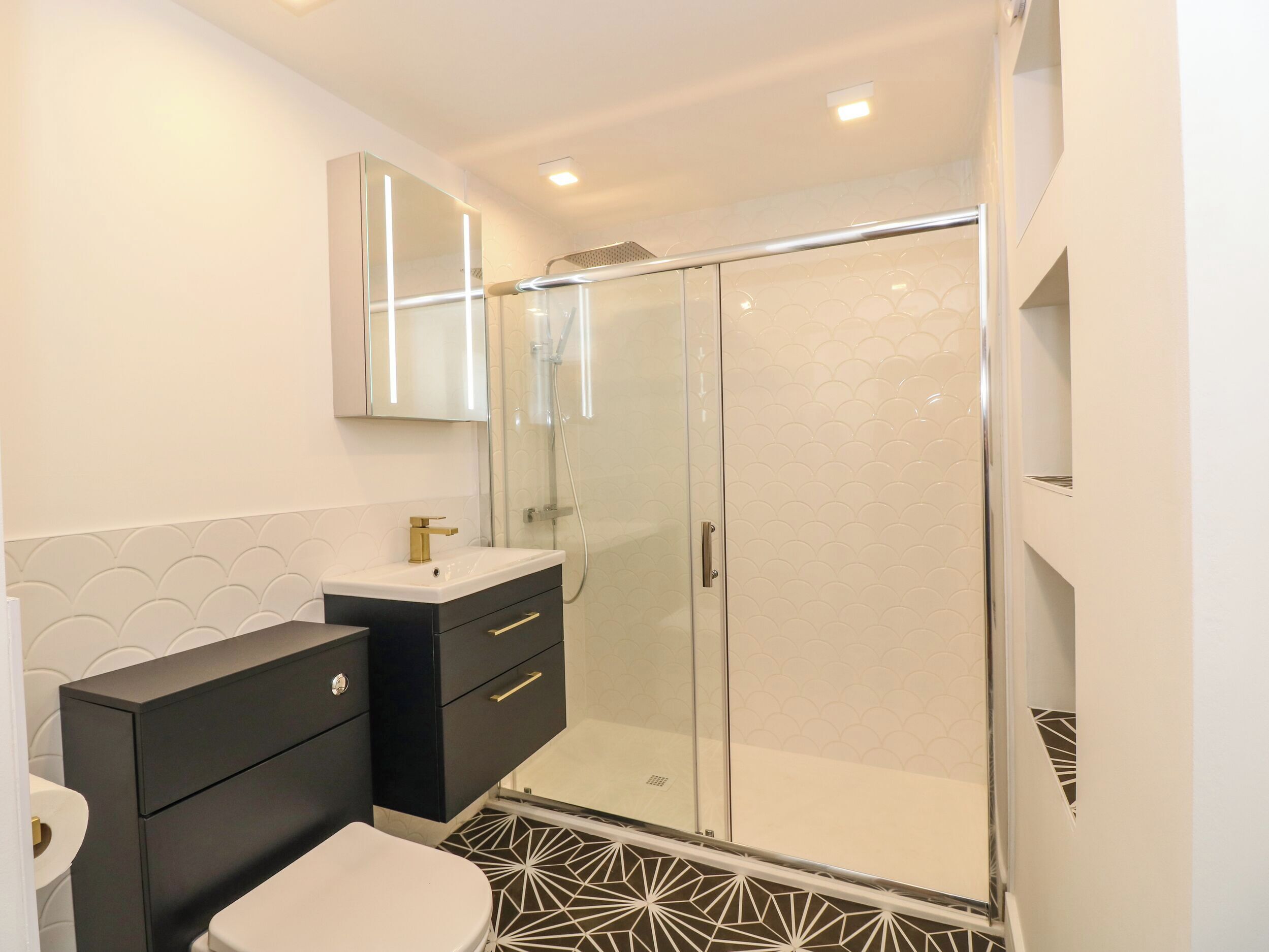 Une salle de bain moderne avec des toilettes blanches, un meuble-lavabo noir et une cabine de douche en verre.