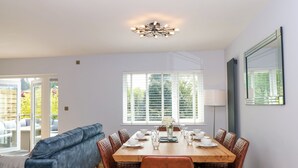 A dining area with a wooden table set for four, surrounded by leather chairs, a blue sofa, and a large window with blinds. - Briars Lea (Windermere)