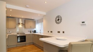 A modern kitchen with wooden flooring, stainless steel appliances, and a white countertop. - Briars Lea (Windermere)