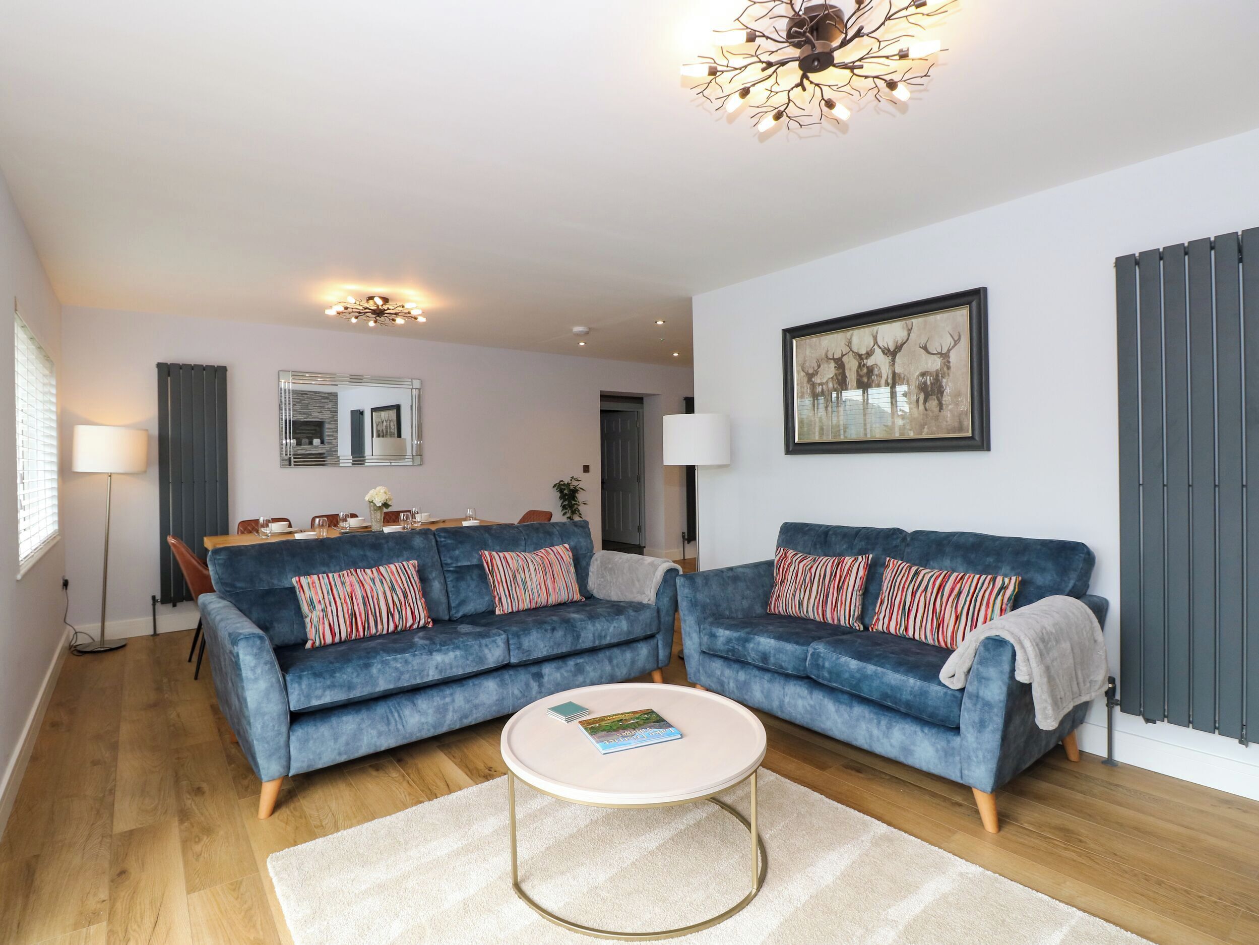 A modern living room with two blue sofas, a round coffee table, and a chandelier.