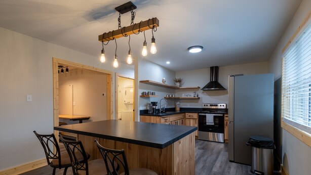 Una cocina moderna con una isla central, taburetes de bar, un refrigerador de acero inoxidable y un horno empotrado.