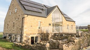 A stone building with a large window and a balcony, surrounded by a stone wall. - Glebe Cottage (Alnwick)