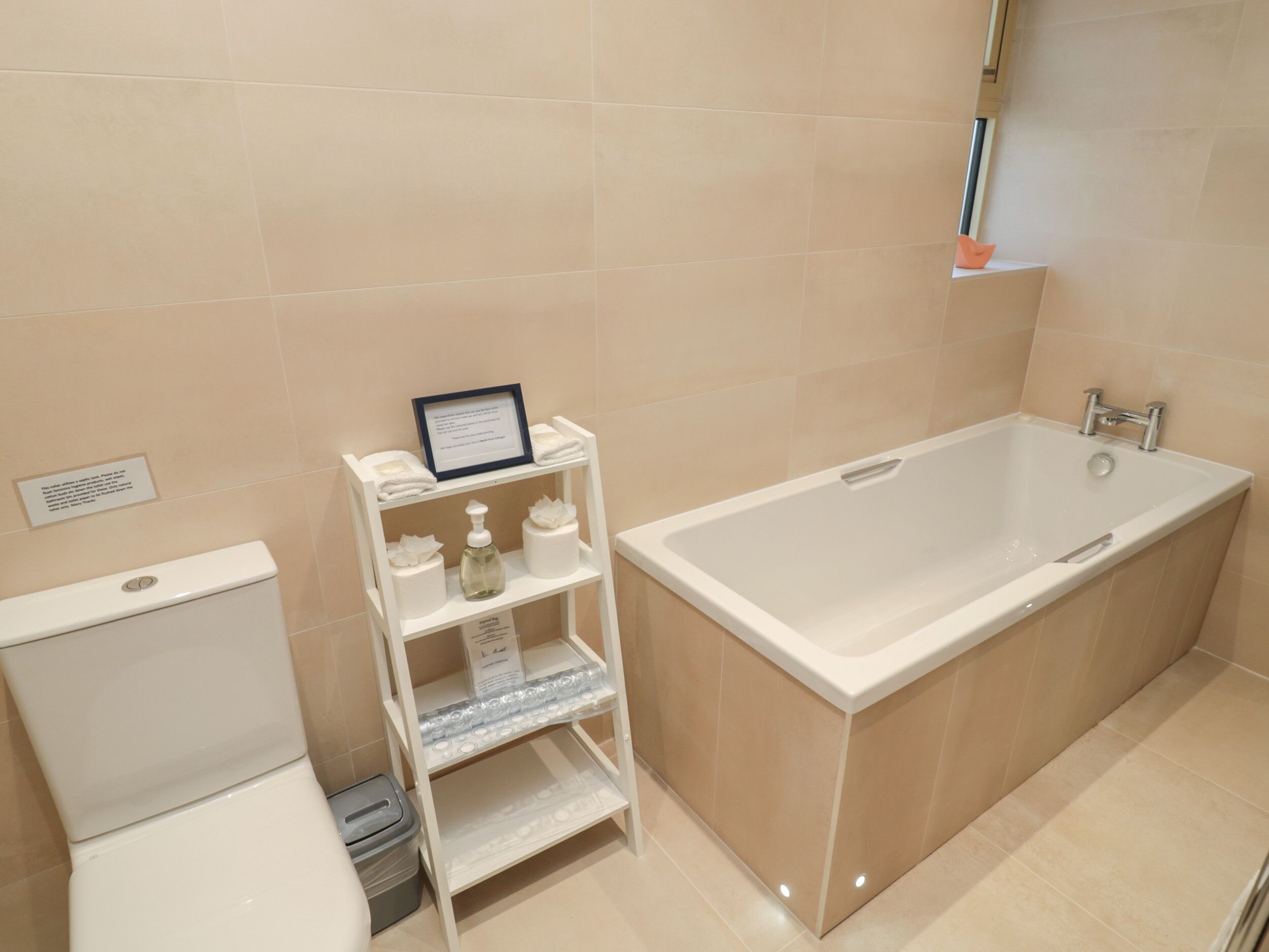 A modern bathroom with a bathtub, toilet, and a shelf with toiletries.