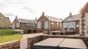 A courtyard with brick buildings, outdoor seating, and a grassy area. - Glebe Cottage (Alnwick)
