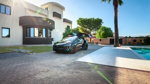 Una casa moderna con un coche en la entrada, piscina y césped cuidado.
