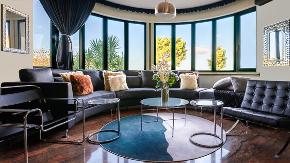 A modern living room with a curved ceiling, large windows, and a black leather sofa.