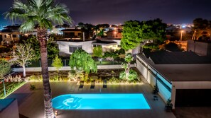 Une piscine sur le toit, illuminée de lumières bleues, entourée de palmiers et bordée d’une architecture moderne.