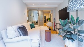 Un salon moderne avec un canapé blanc, une petite table d’appoint ronde et une grande plante en pot.
