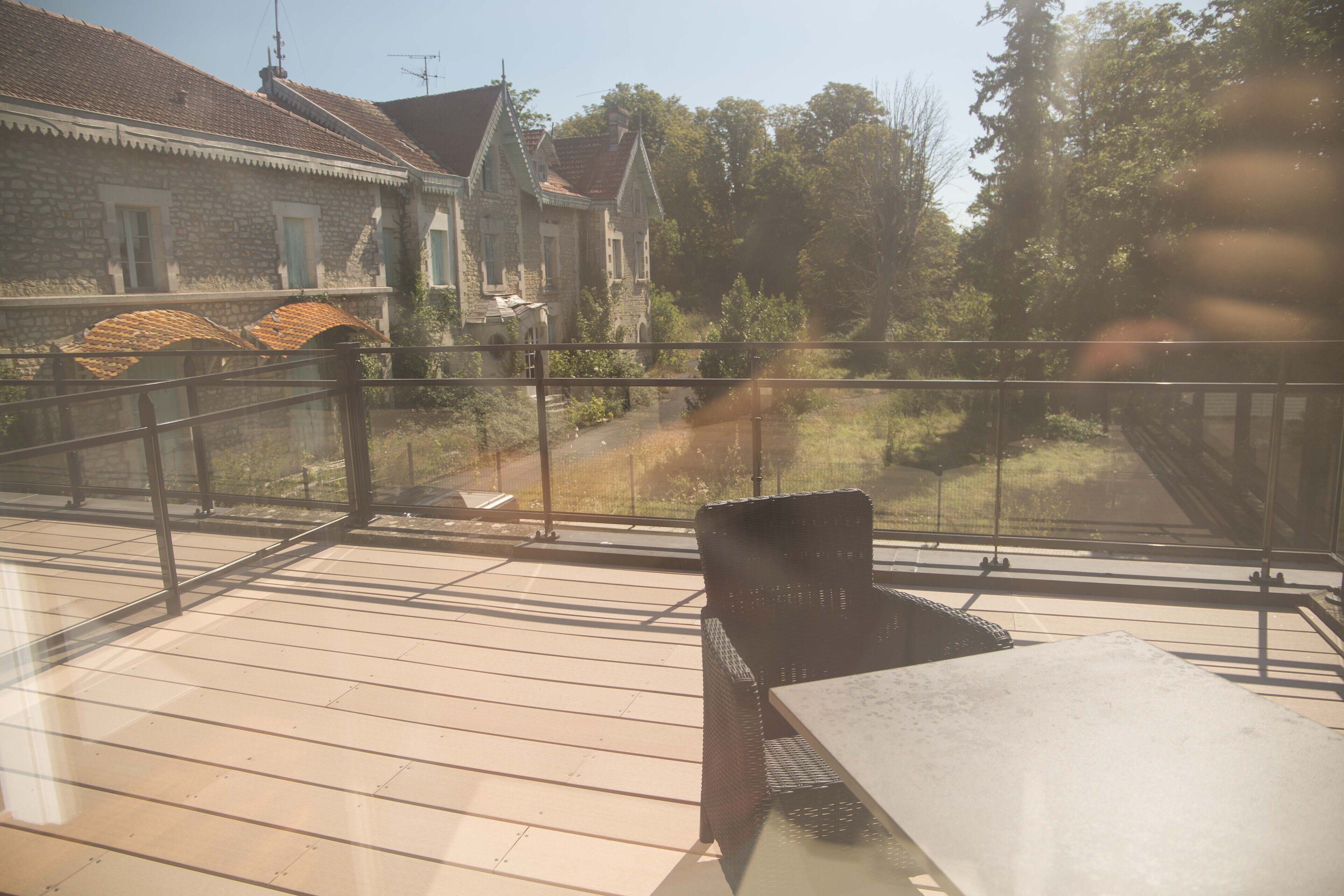 A wooden deck with a table and chairs, overlooking a stone building with a tiled roof.