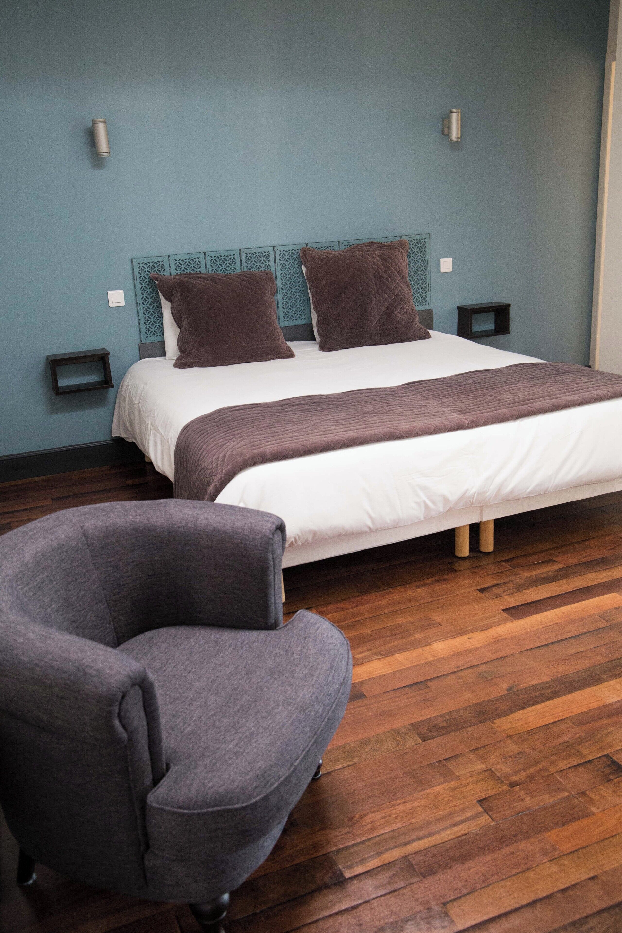 Un dormitorio moderno con una cama grande, dos mesitas de noche, una silla y suelo de madera.